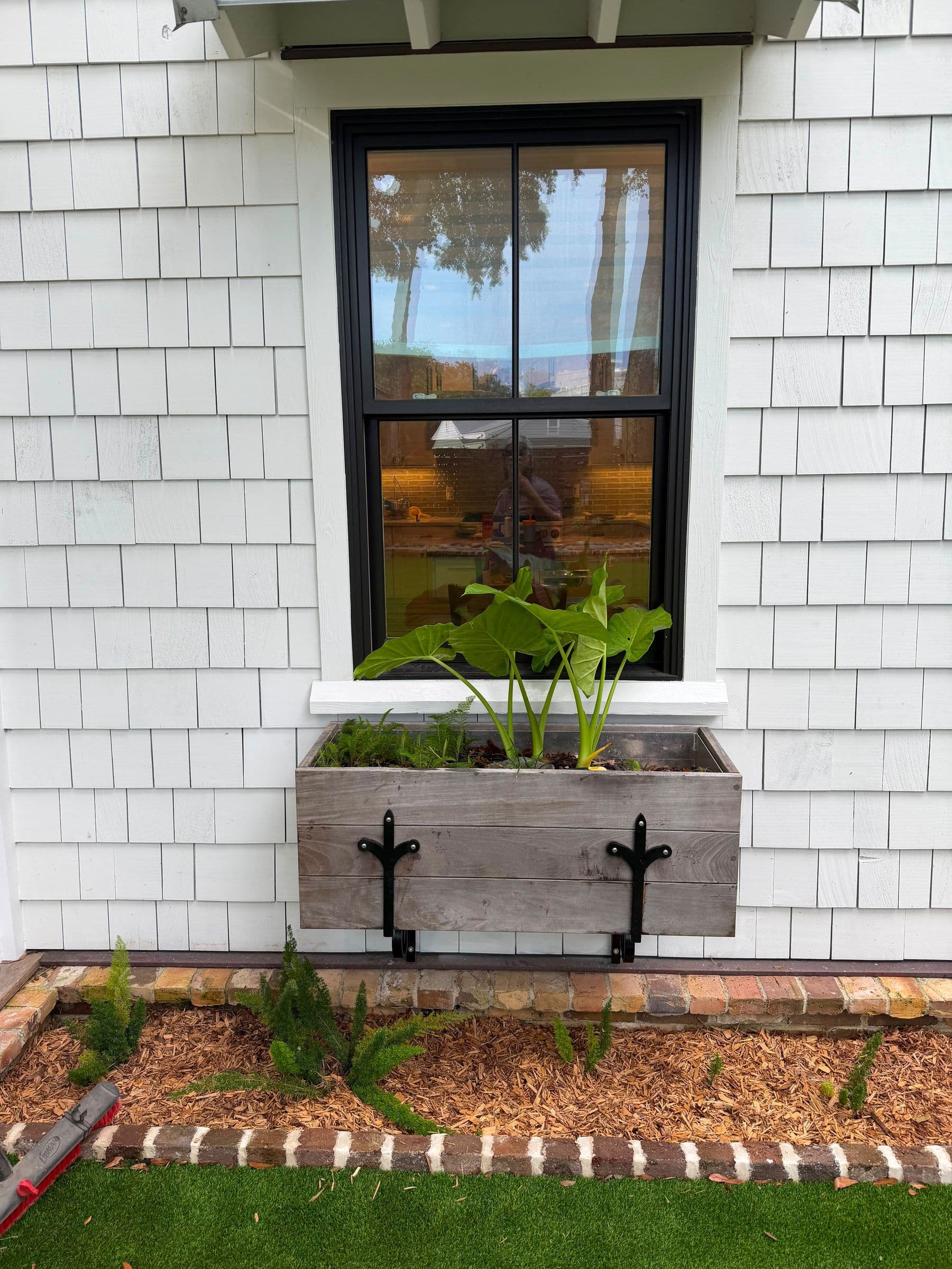 Cedar window box under a black double-hung window in white shake siding