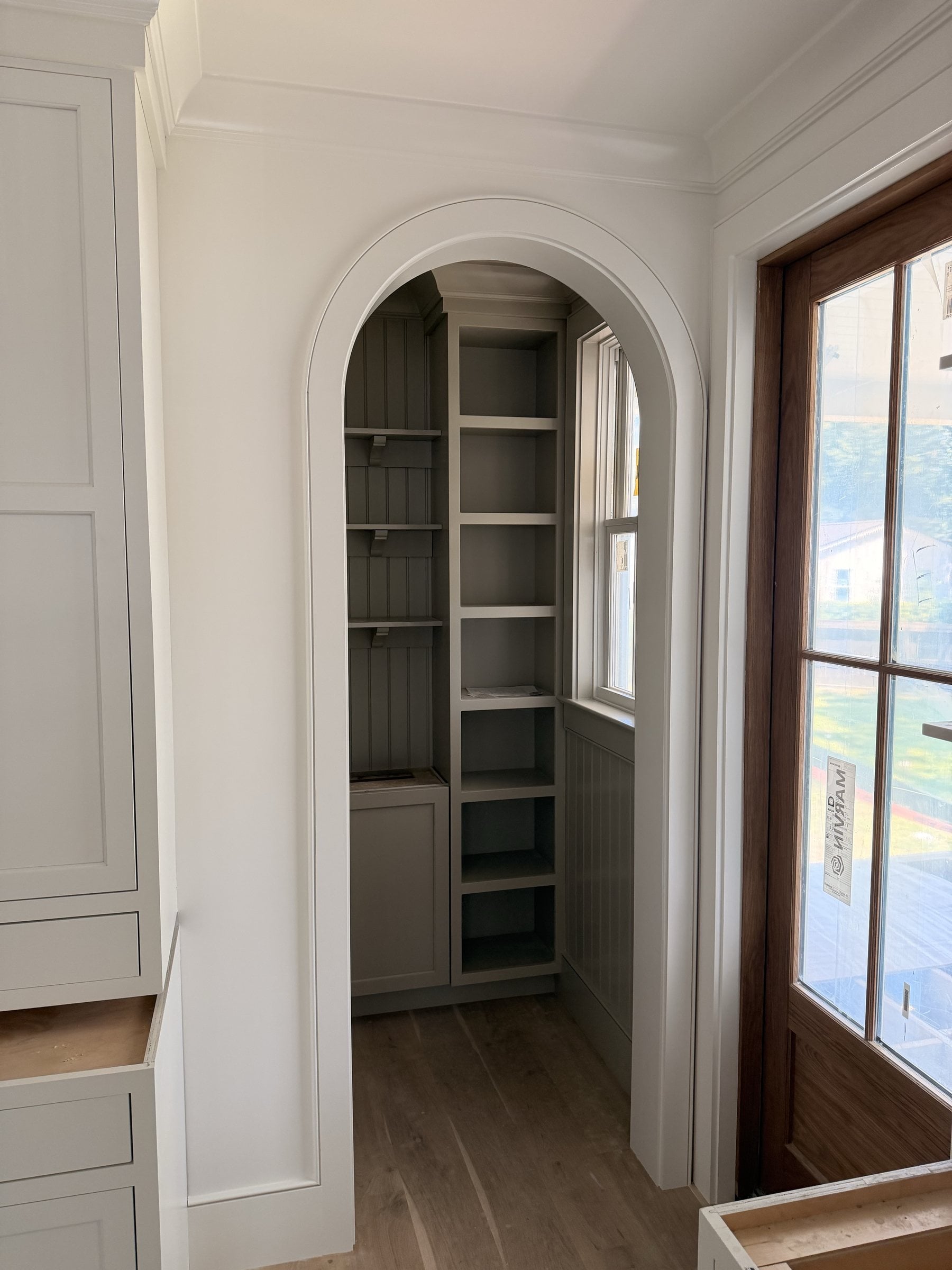 Arched pantry opening beside painted kitchen cabinetry and a wood door