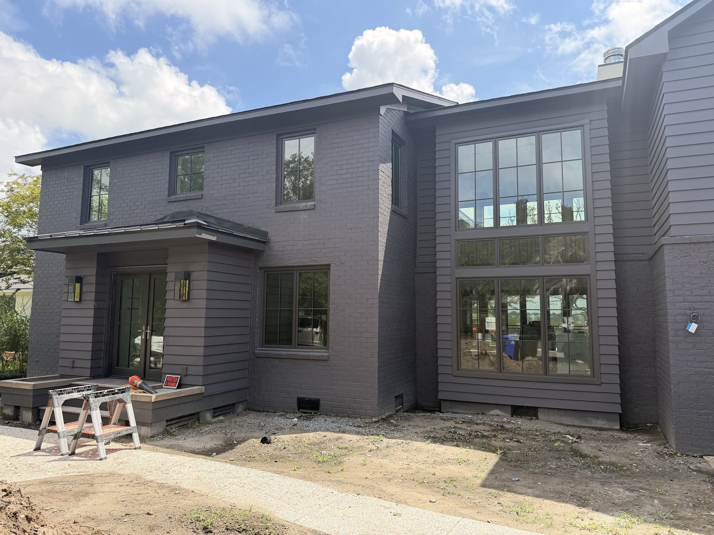 Two-story house in painted brick and dark lap siding with a two-story window wall
