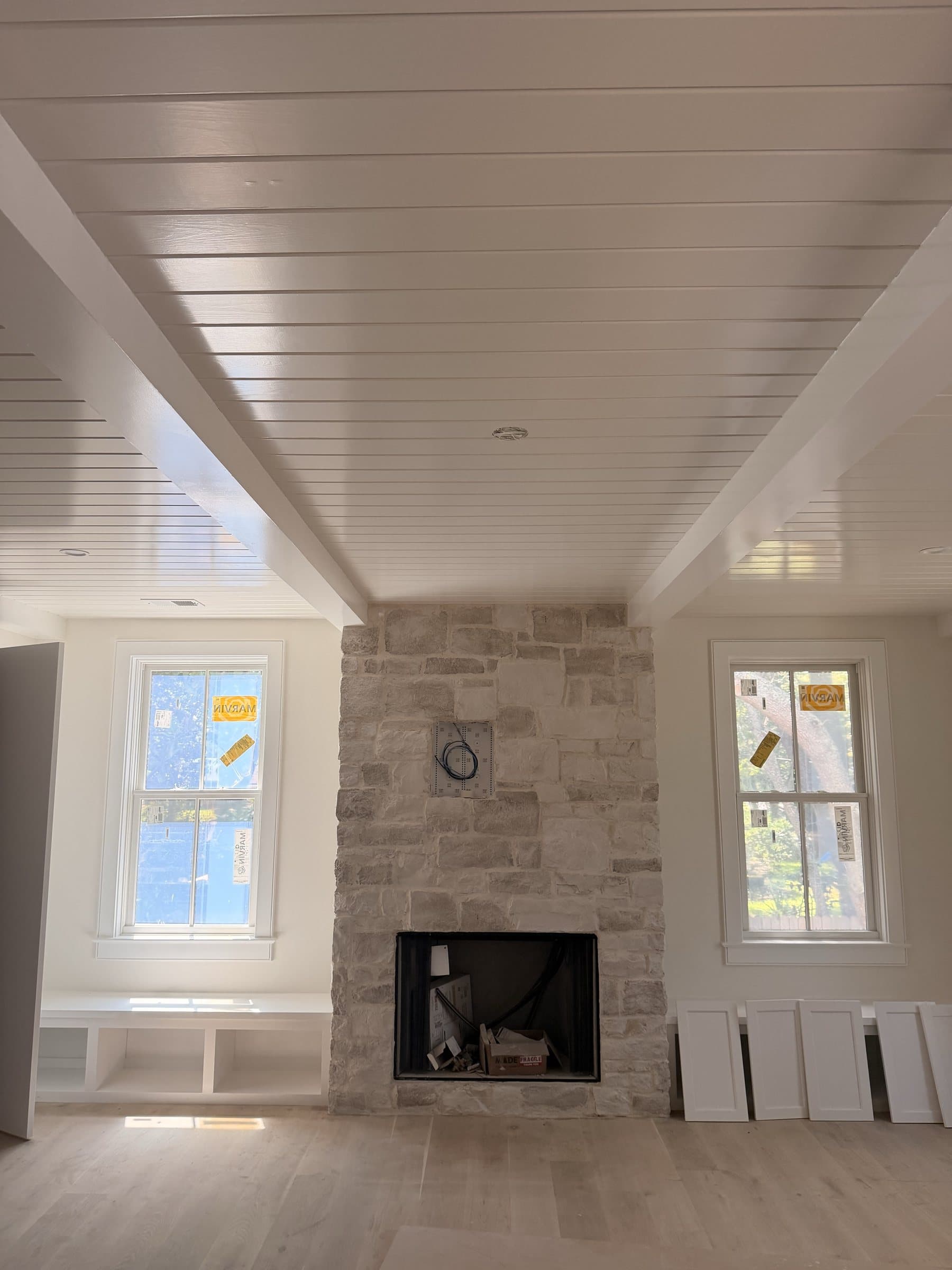 Stone fireplace between windows under a beadboard ceiling with cased beams