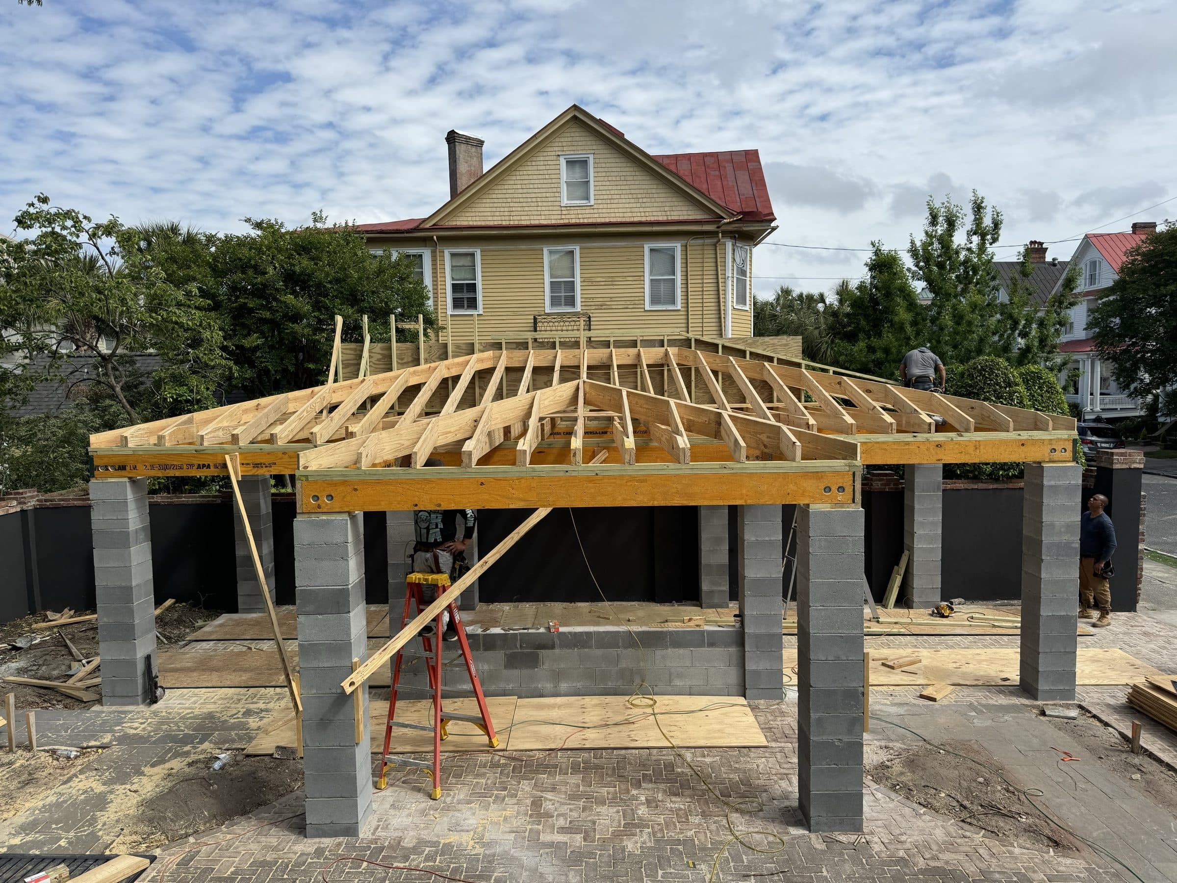 Hip-roof pavilion framed over block piers beside a house