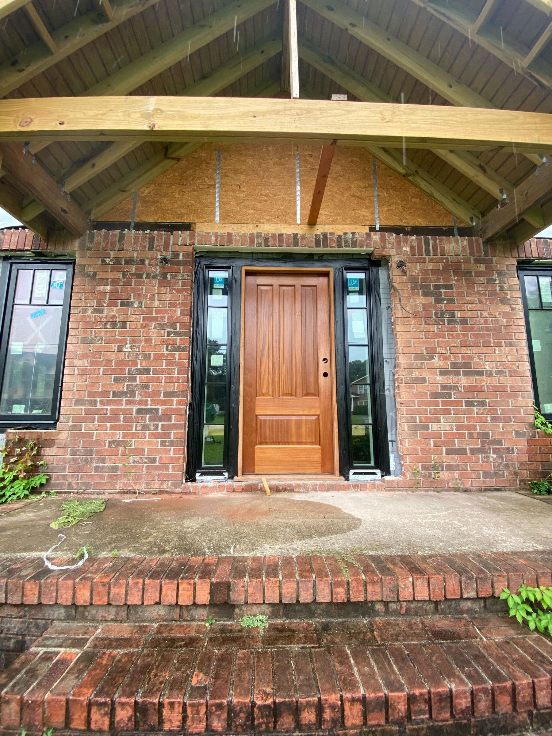 Mahogany entry door with sidelights under a timber porch roof