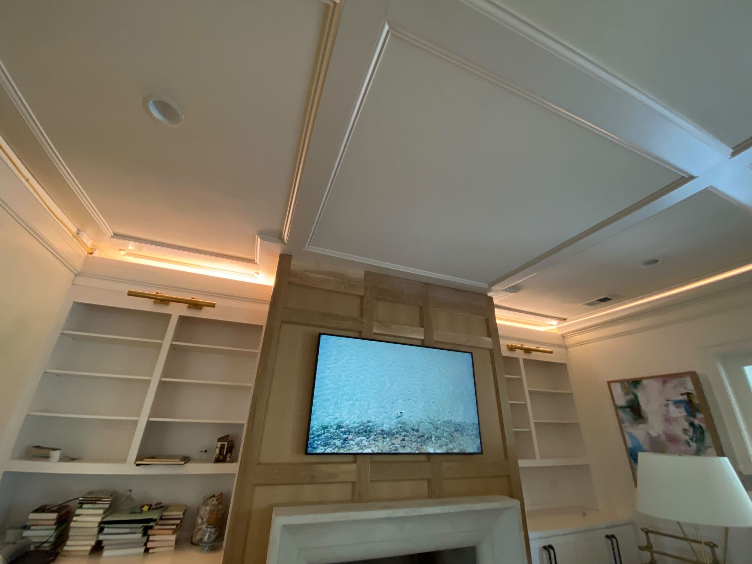 Oak-paneled media wall with flanking built-in shelves under a coffered ceiling