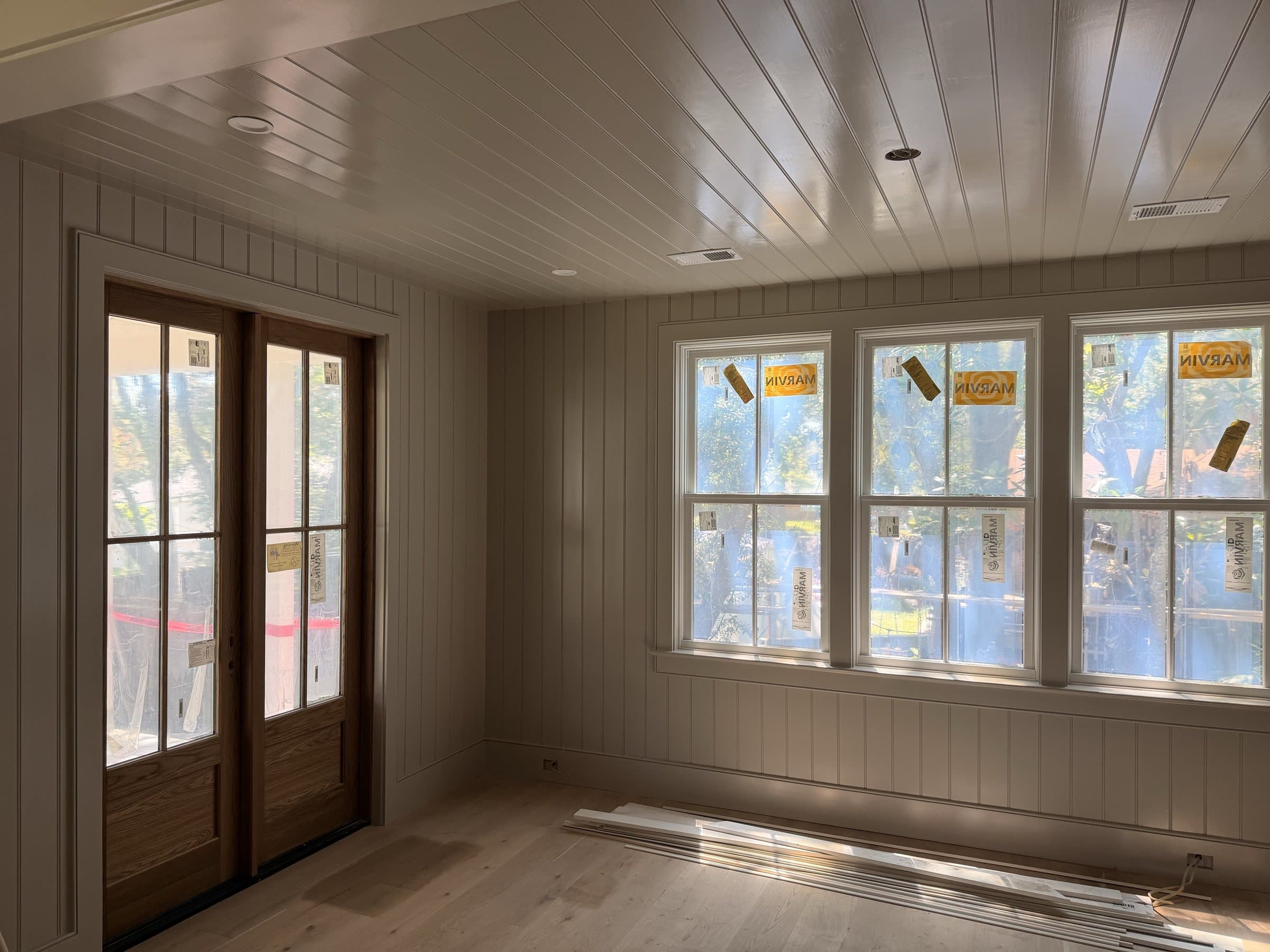 Room finished in vertical paneling with a beadboard ceiling, wood French doors and triple windows