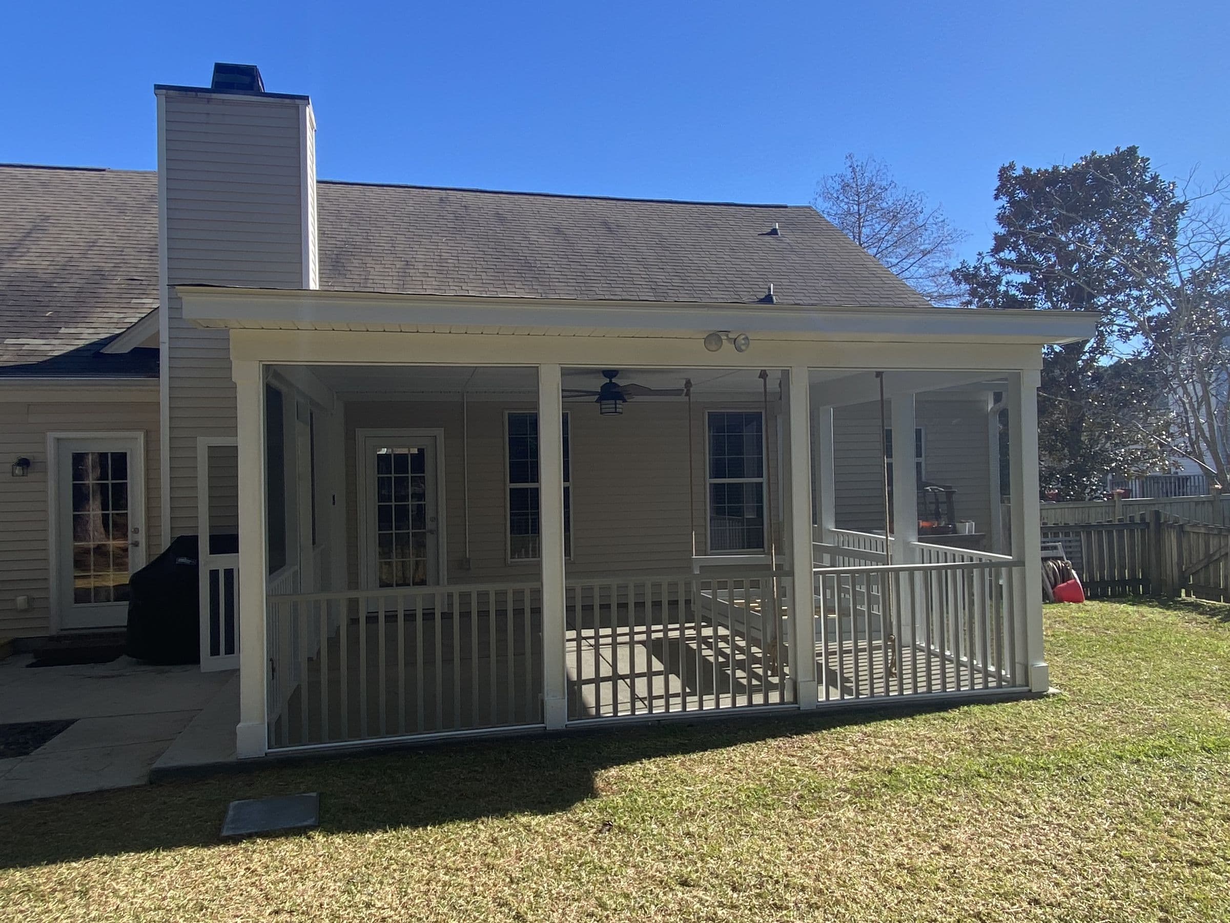 Screened porch addition on a brick home, built with white rails and a shingled roof
