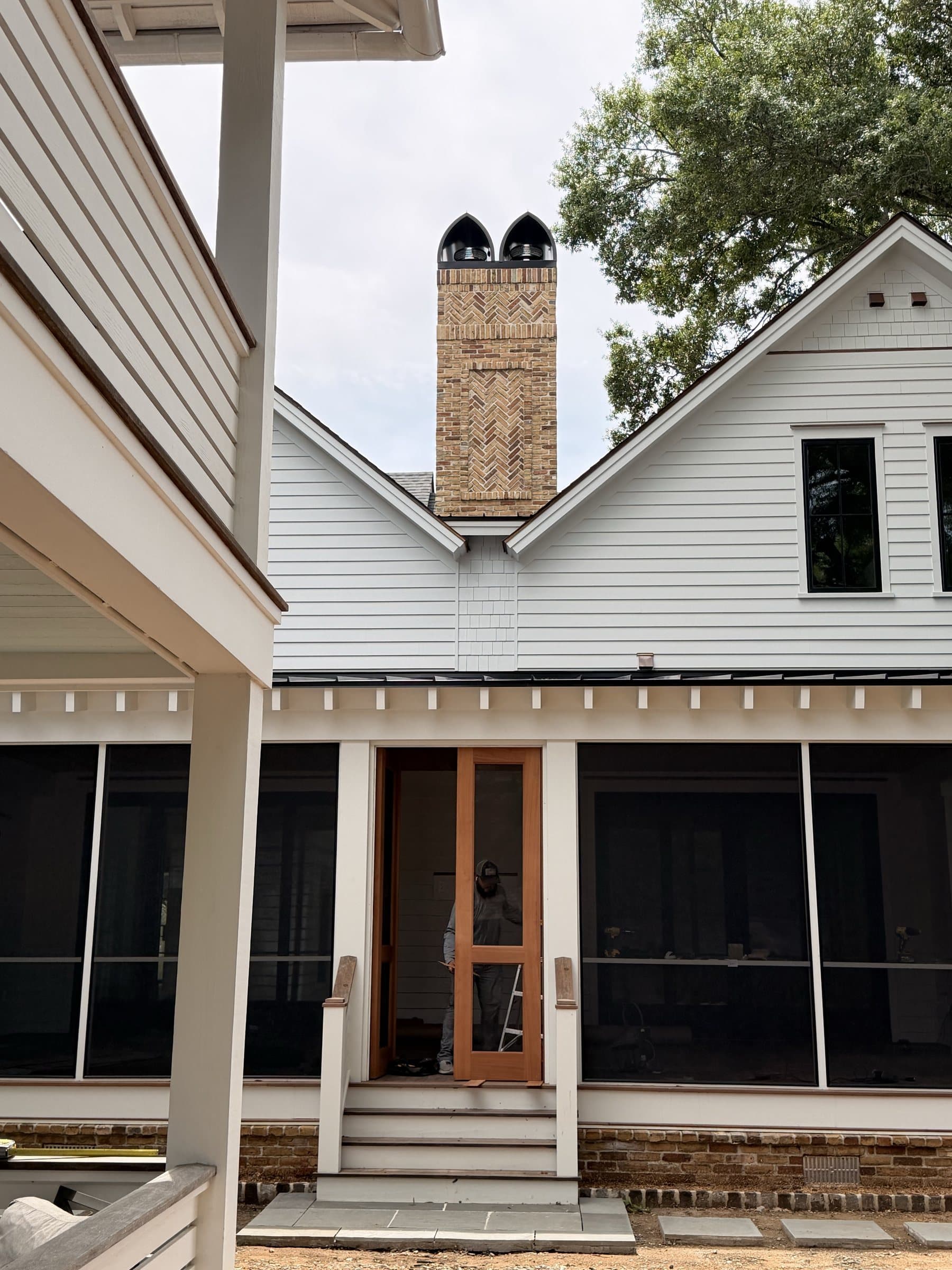 Screened porch with a wood screen door under a herringbone brick chimney