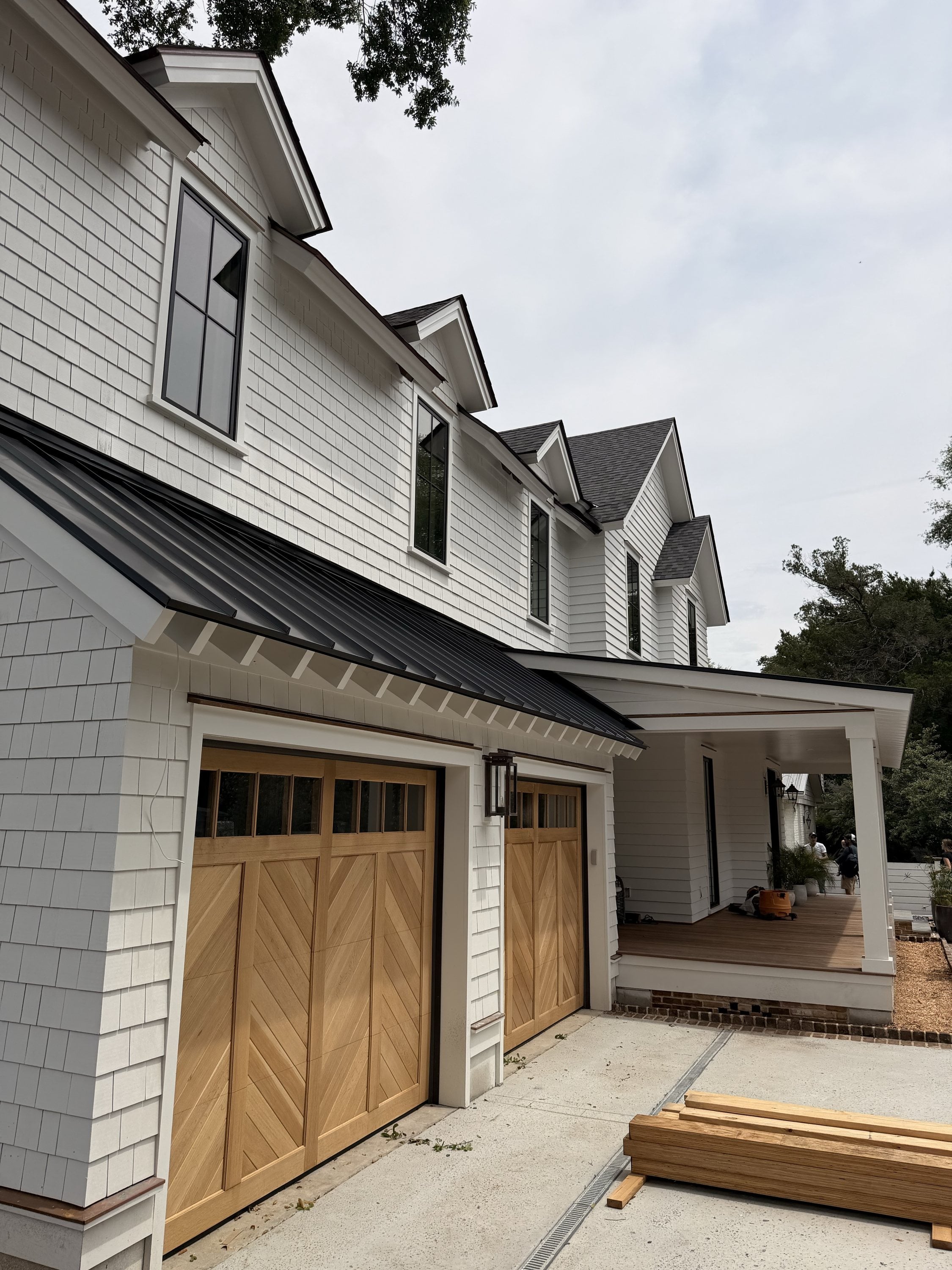 White shingle house with dormers, a standing-seam porch roof and wood carriage garage doors