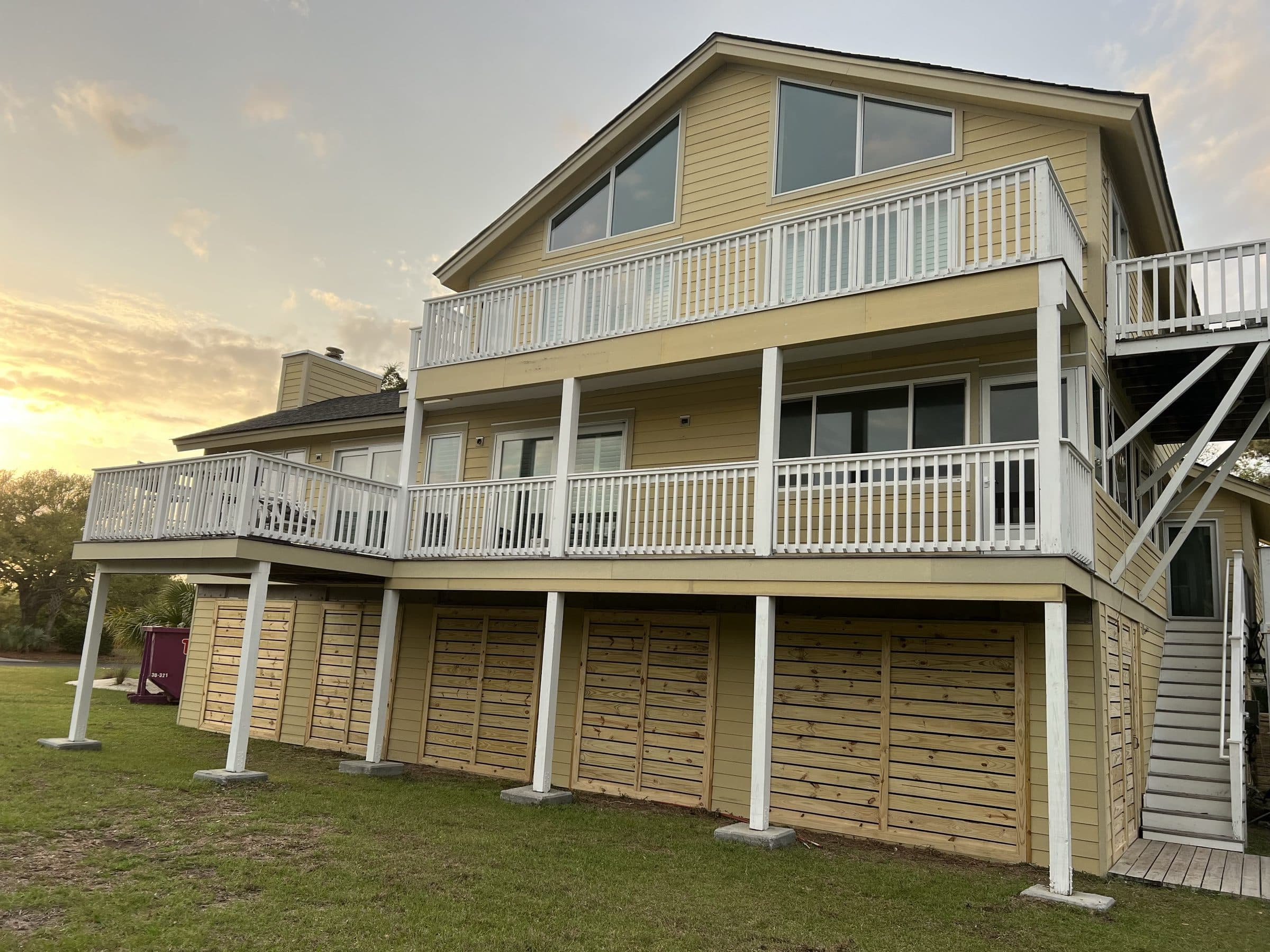 Three-story house re-sided in yellow lap siding with stacked porches at sunset